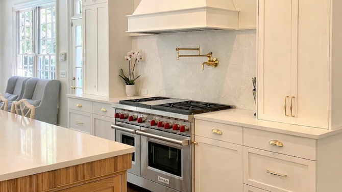 Modern white kitchen with gold hardware, a large gas range, and a marble backsplash.