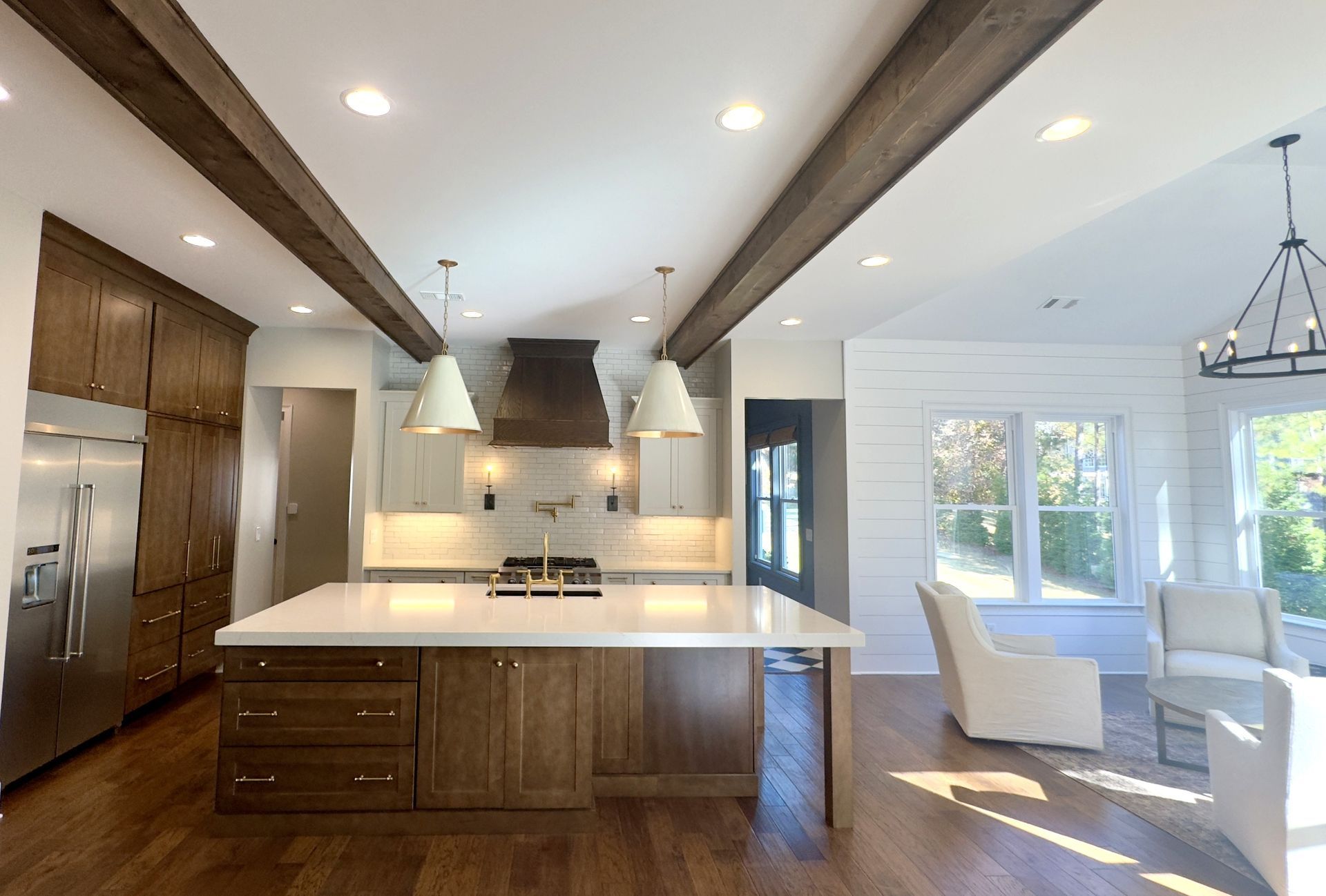 Modern kitchen with wood beams, island, and adjacent living space with white walls and natural light.