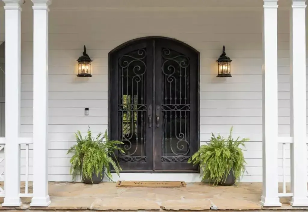White porch with ornate black doors, ferns, and hanging lanterns.