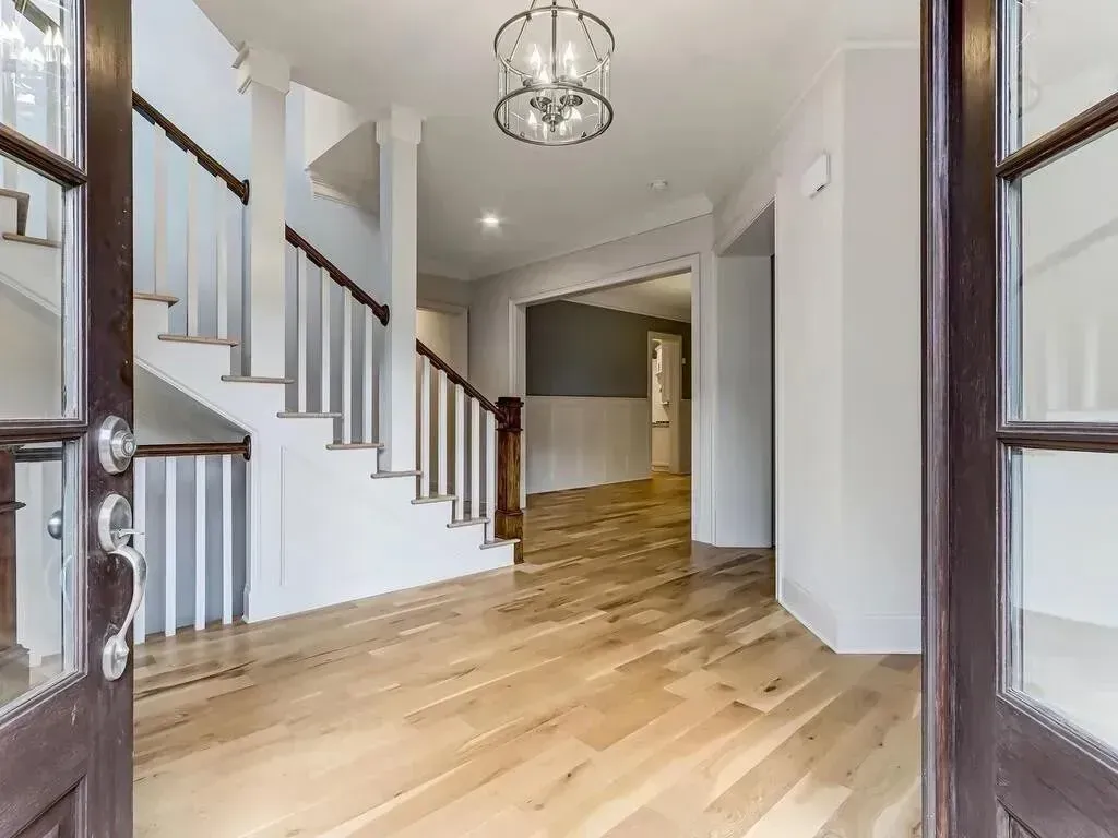 Entryway with wooden floors, staircase, chandelier, and open doorway.