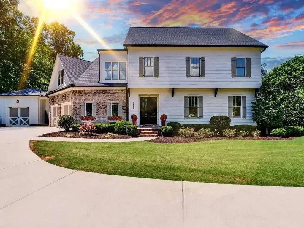Two-story white house with brick accents, shutters, and a green lawn under a sunny sky.