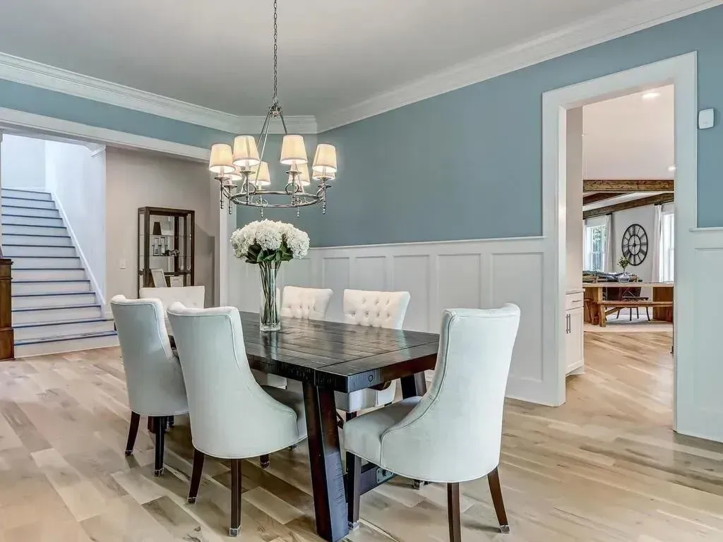 Elegant dining room with a dark table, white chairs, and a chandelier; light blue walls.