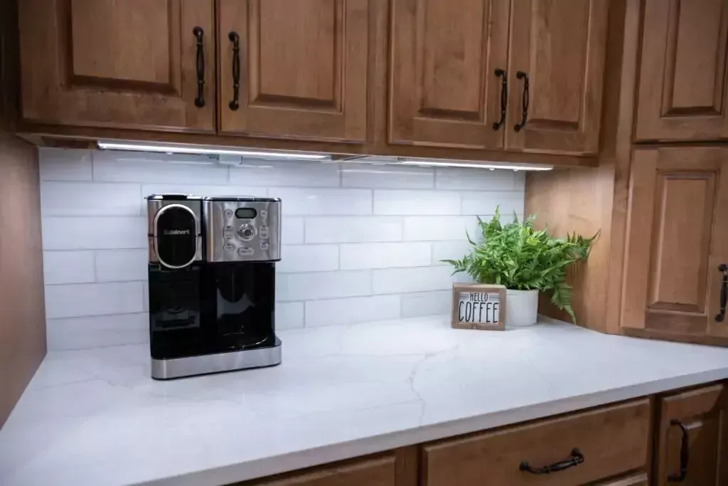 Coffee maker on white countertop in a kitchen with wooden cabinets and subway tile backsplash.