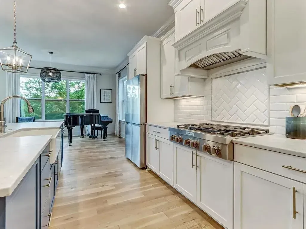 Modern kitchen with white cabinets, stainless steel appliances, and a piano in the background.