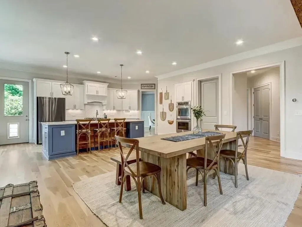 Open-concept kitchen and dining area with blue island, wooden table, and chairs. Light wood floors and white cabinetry.