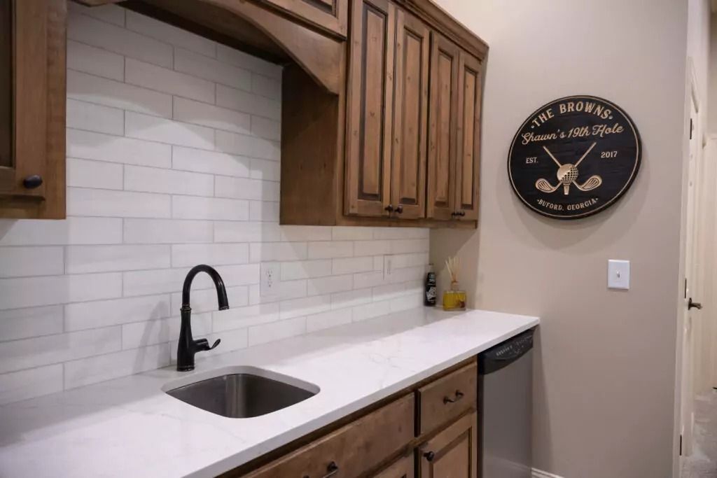 A small kitchen with brown cabinets, white countertop, black faucet and sink, and a golf-themed clock on the wall.
