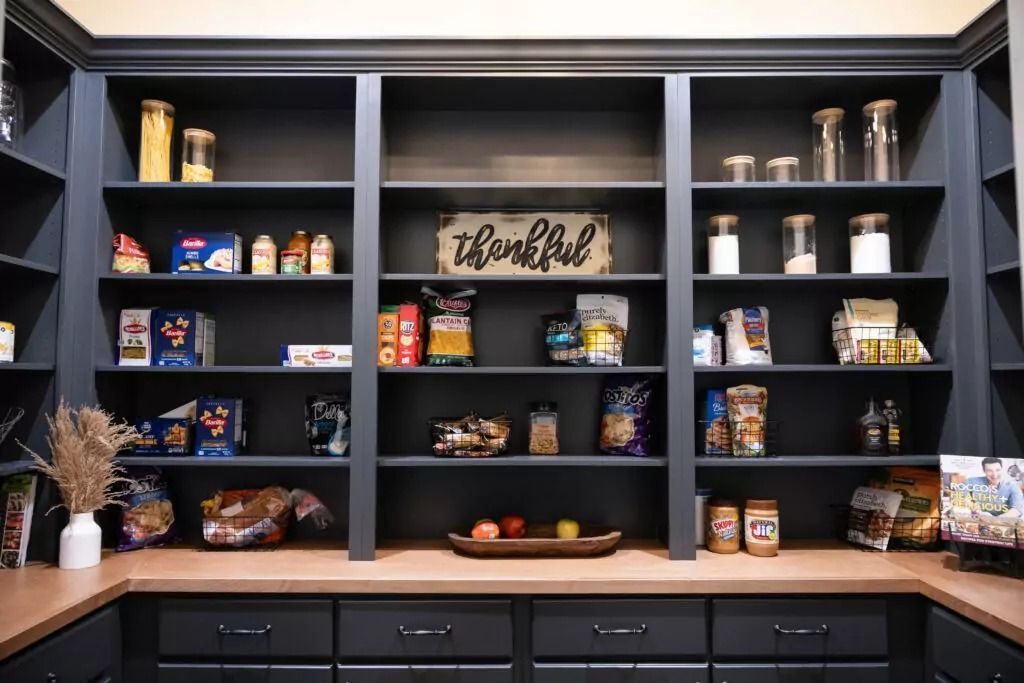Dark pantry shelves filled with food items, drawers below. Wooden sign: 