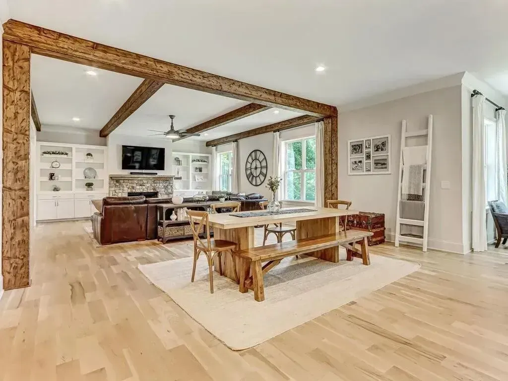 Open-concept living space with exposed wooden beams, dining table, and built-in shelves.