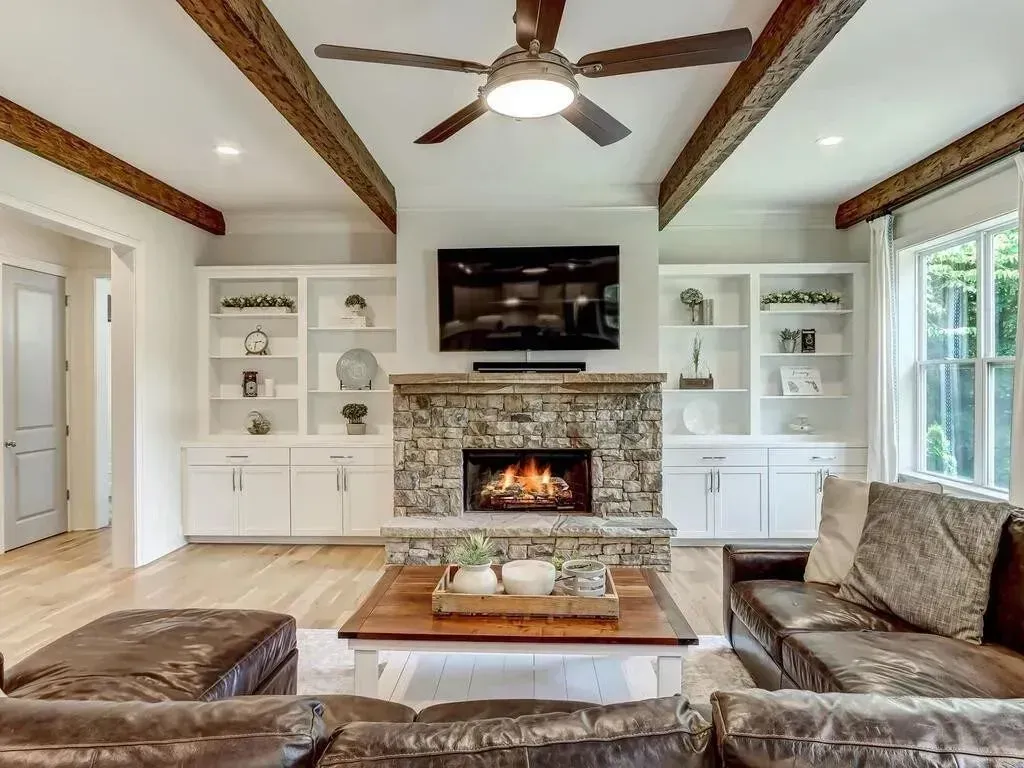 Living room with fireplace, built-in shelves, wood beams, and leather furniture.