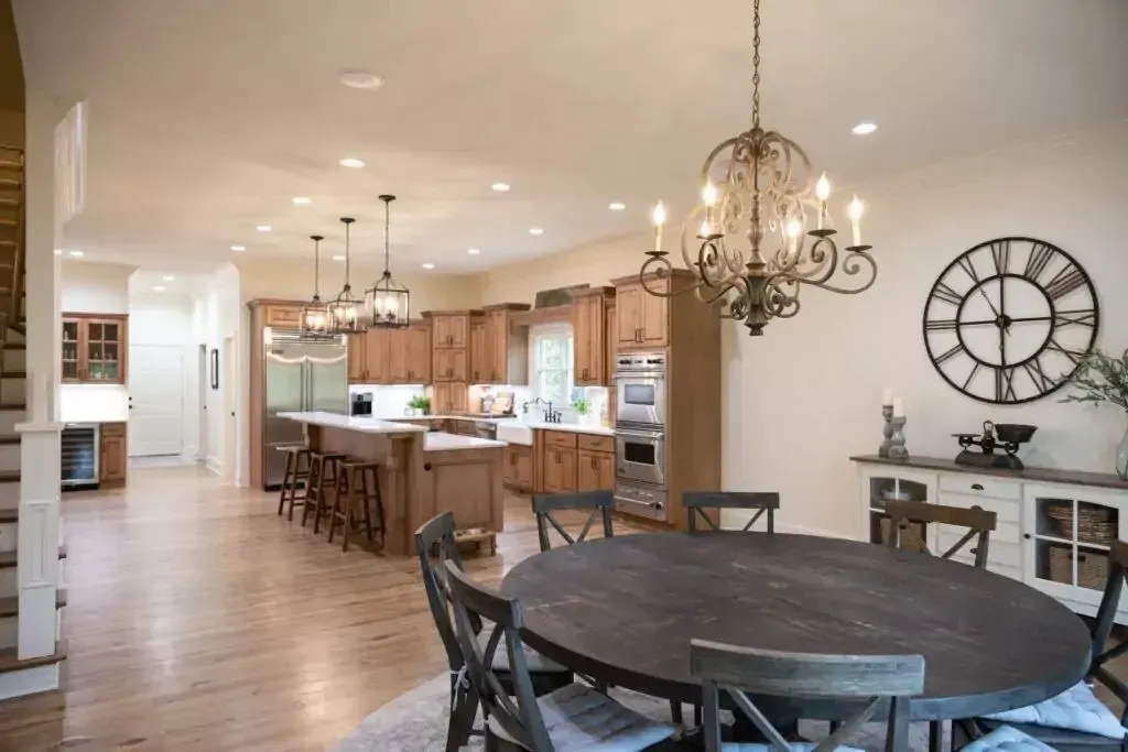 Open-concept kitchen and dining area with wood cabinets, island, table, and chandelier; clock on the wall.