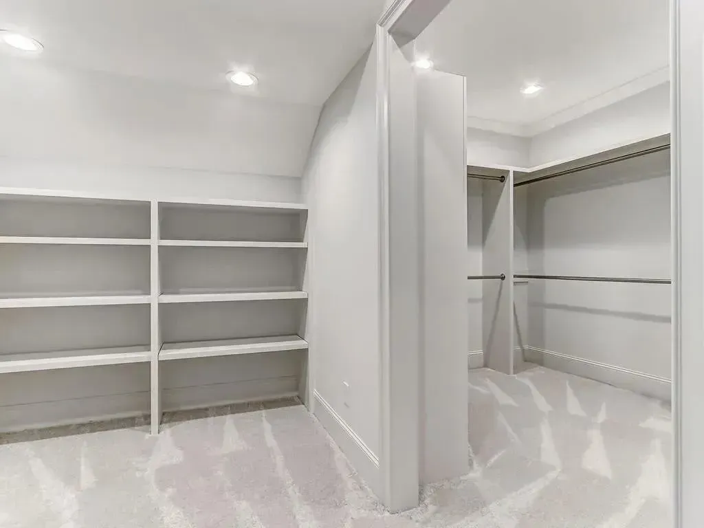 White walk-in closet with shelves and rods, on a fluffy white carpet.
