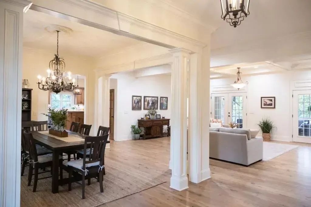 Spacious interior with dining table, pillars, and chandelier lighting. Wooden floors and open layout.