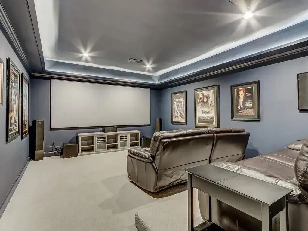 Home theater with a large screen, black seating, and movie posters on blue walls.