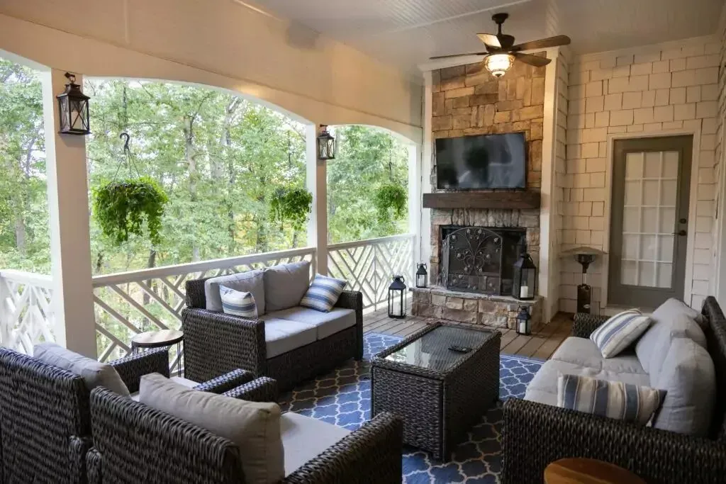 Covered outdoor living space with furniture, fireplace, and wooded view.