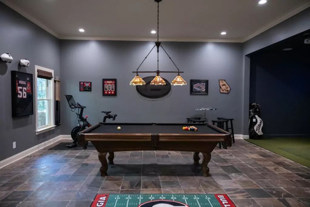 Pool table in a game room with sports memorabilia, a stationary bike, and a golf simulator.