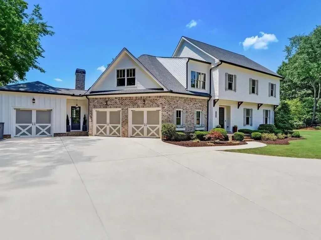 Two-story white house with brick accents, gray roof, and attached garages on a sunny day.