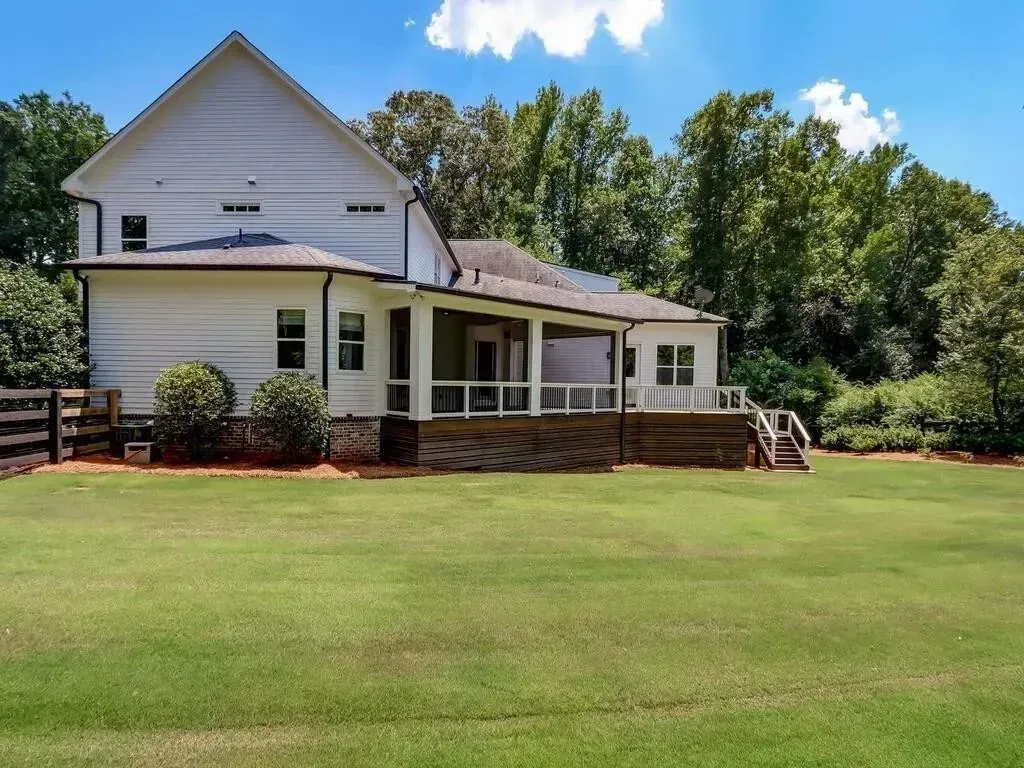 White house with a screened porch and deck, surrounded by green grass and trees on a sunny day.