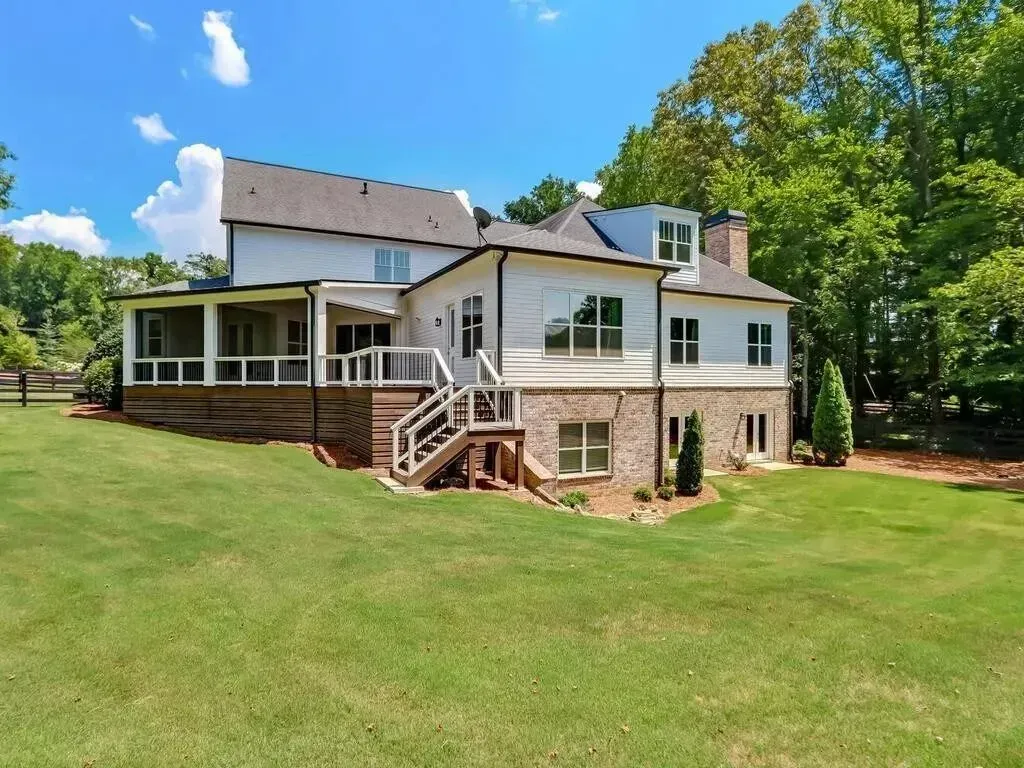 Two-story white house with a screened porch, brick details, and green lawn on a sunny day.