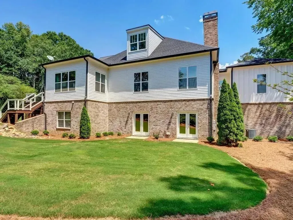 Rear view of a two-story house with a brick base, white siding, and a green lawn.