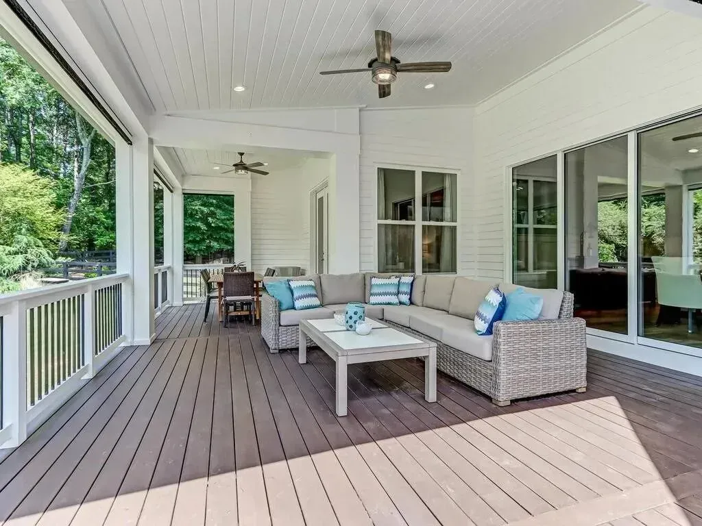Covered outdoor patio with wicker sectional, coffee table, and ceiling fans. Brown wood floor, white trim, and views to the outside.