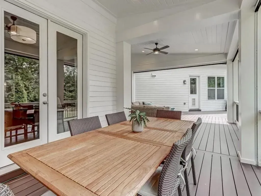 Outdoor dining area with large wooden table and chairs on a covered porch.