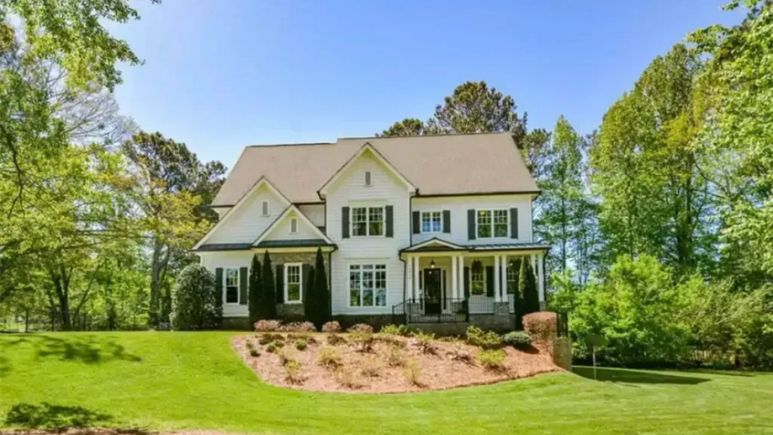 White two-story custom home with green lawn, trees, and blue sky in Milton Ga
