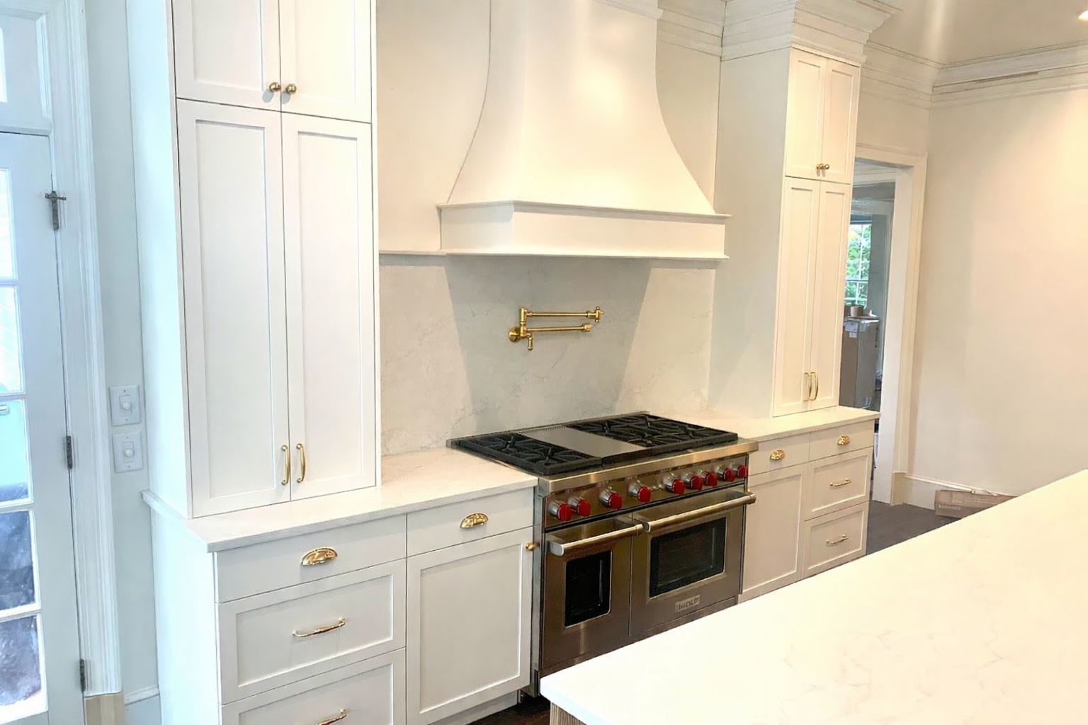 White kitchen with stove, range hood, cabinets, and a kitchen island.