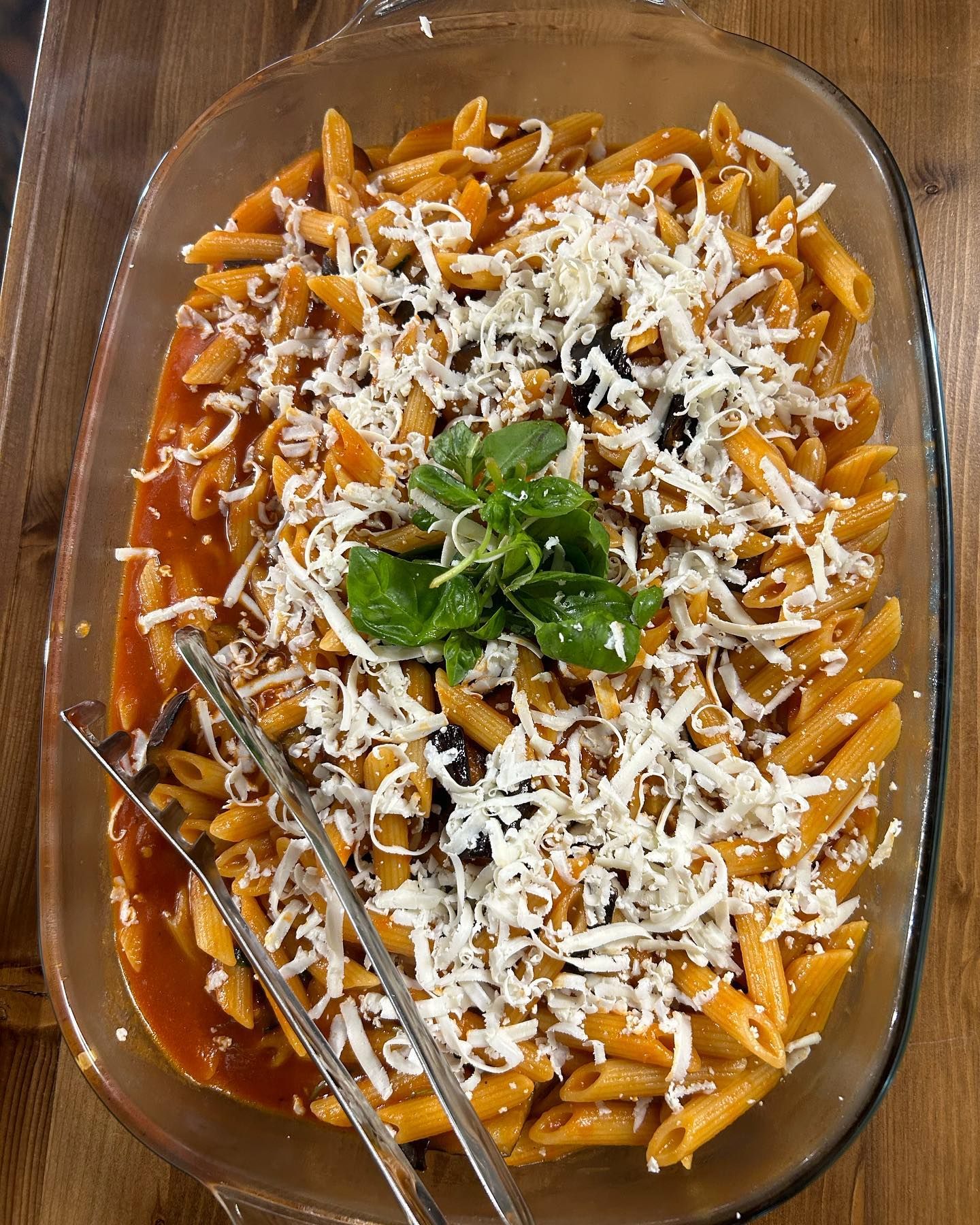 Pasta al forno in una pirofila di vetro, guarnita con formaggio grattugiato e basilico fresco.