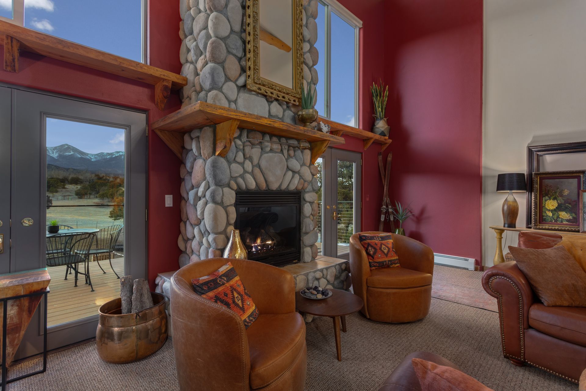 Living room with stone fireplace, two brown leather sofas, large windows, and a rug.