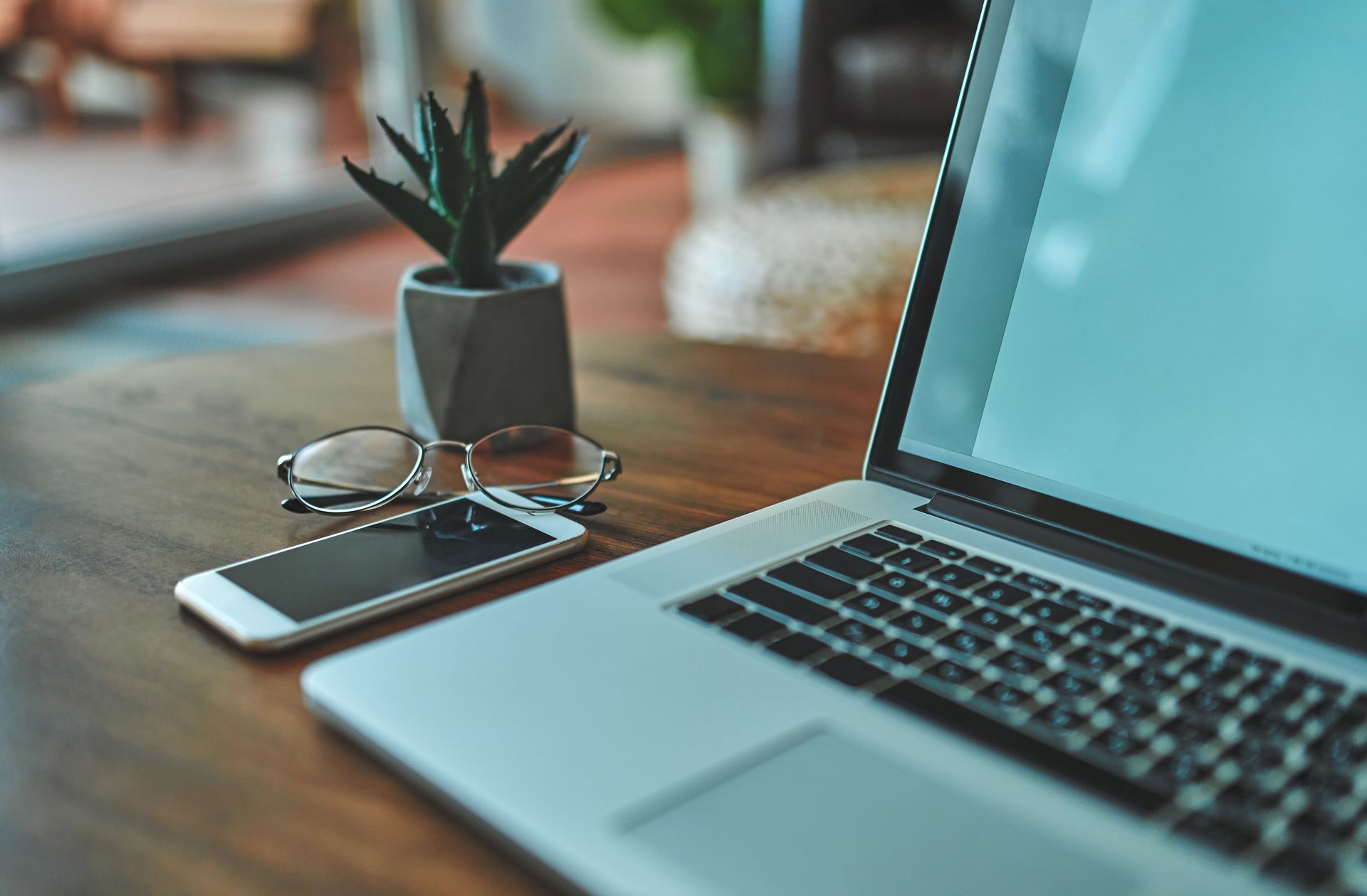 Person typing on laptop outdoors at a wooden table with a phone, notebook, and coffee.