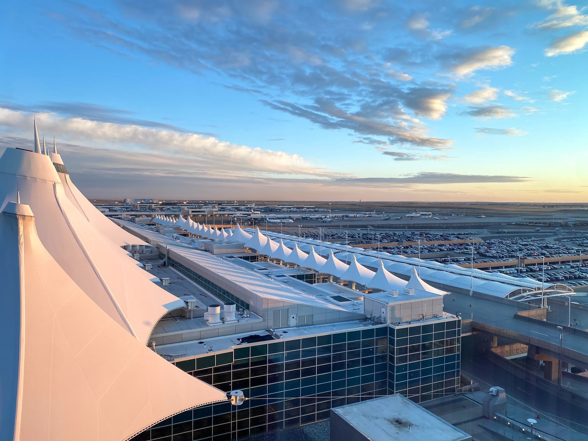 Airplane wing in flight, above a sea of white clouds, against a blue sky.