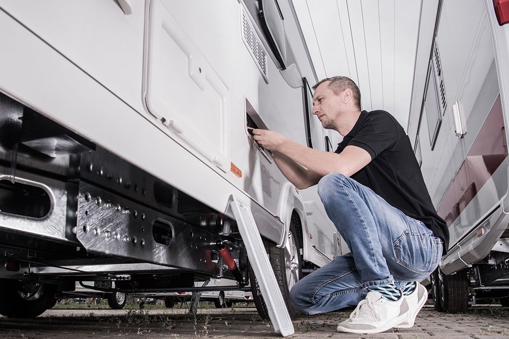 A man is kneeling down next to a rv.