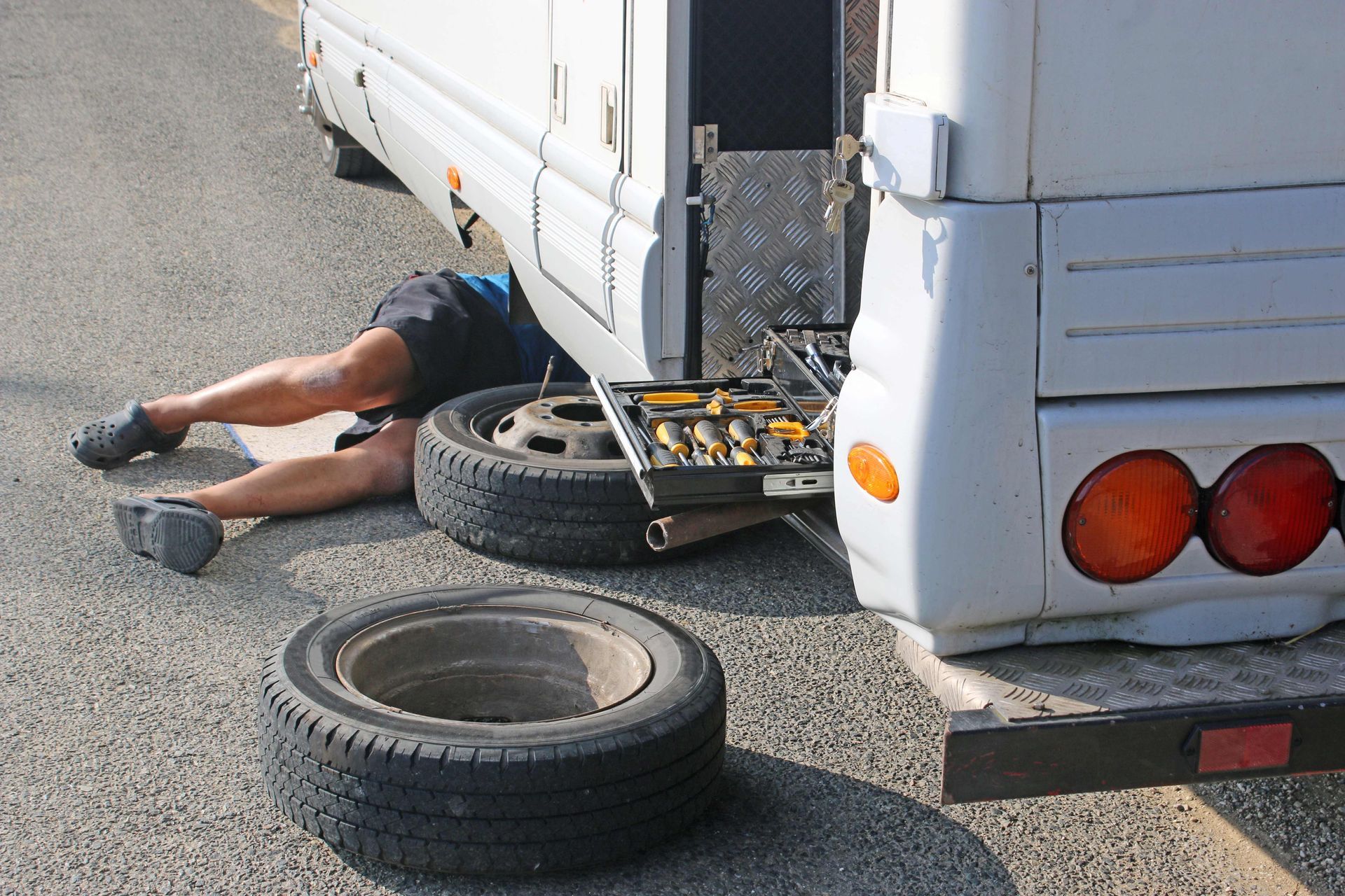 Technician performing mobile RV repair services under a motorhome beside a spare tire and tool kit. Technician performing mobile RV repair services under a motorhome beside a spare tire and tool kit.
