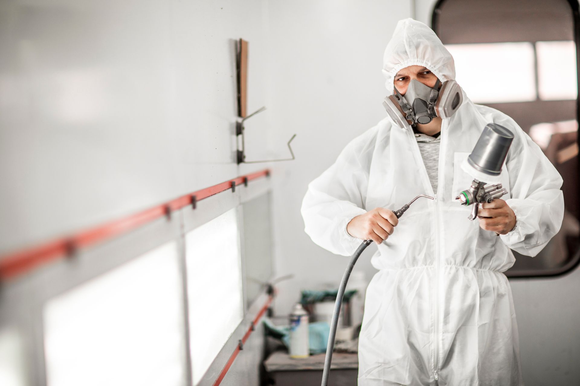 RV painter in white coveralls using spray gun inside a paint booth for RV services.