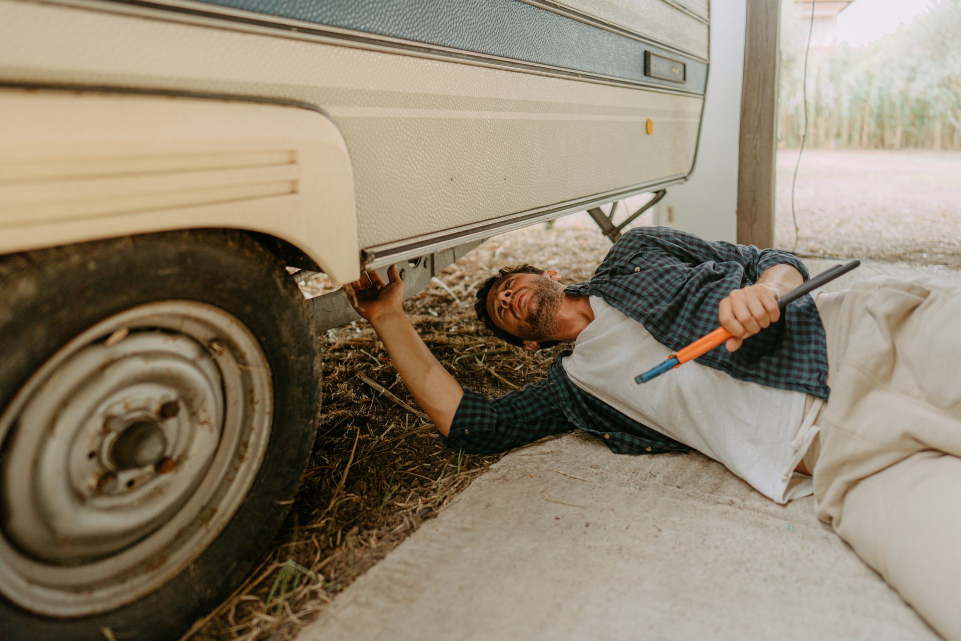 A man repairing and checking a recreational vehicle lying on the ground with a wrench.