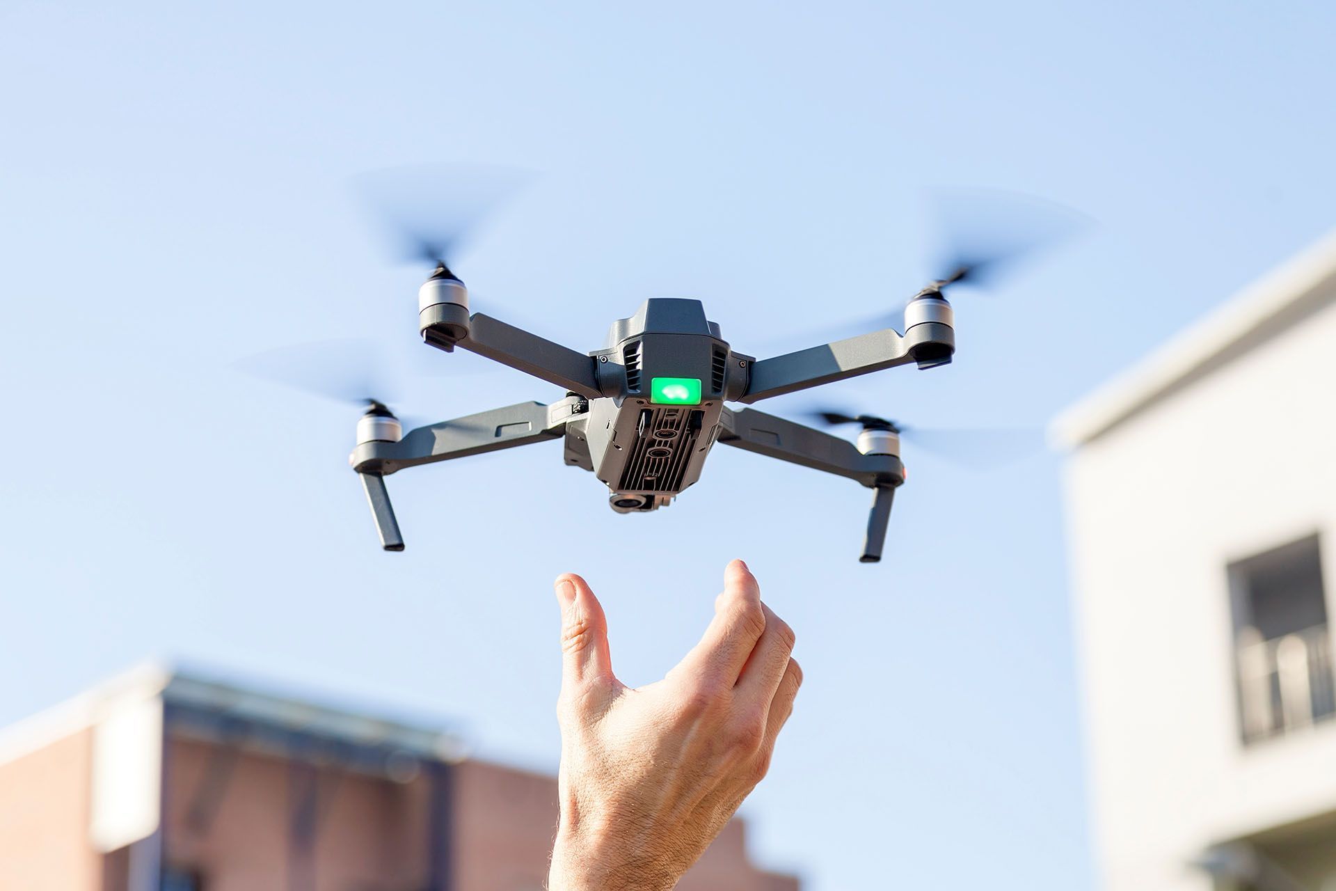 Drone hovering over hand reaching up, against a blue sky.