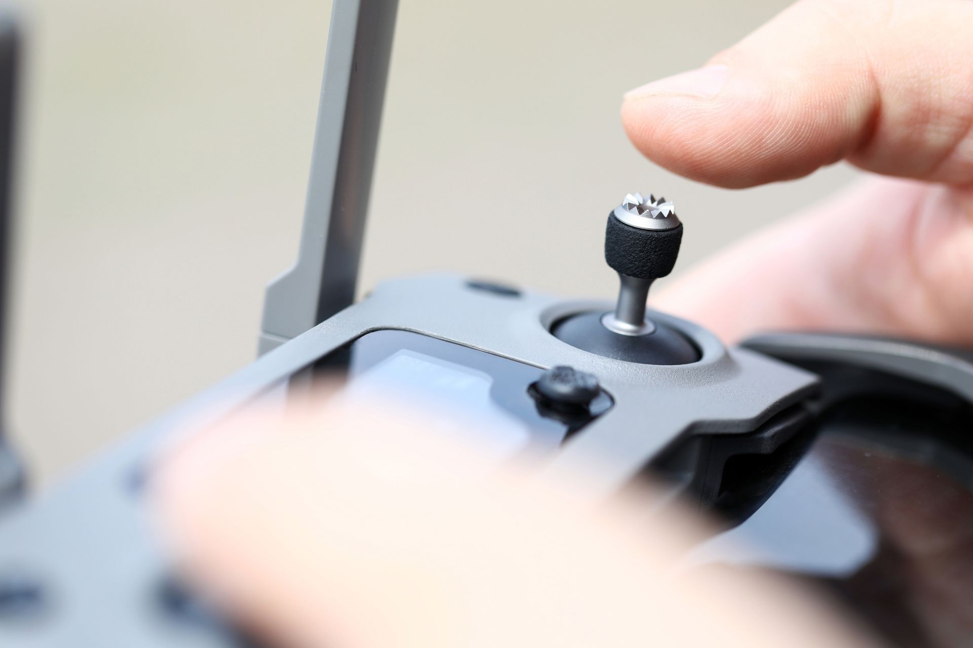 Hand operating a drone remote control, with focus on the joystick and screen.