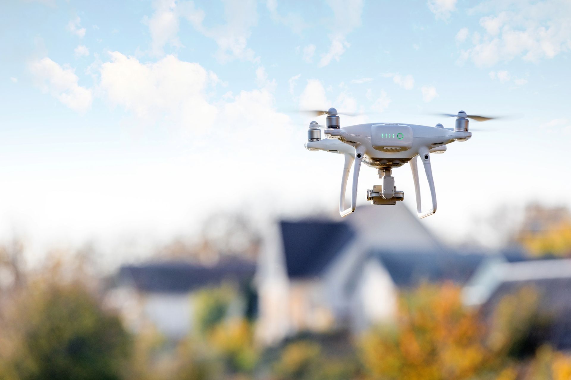 Drone in flight over a suburban neighborhood with blue sky and some trees in the background.