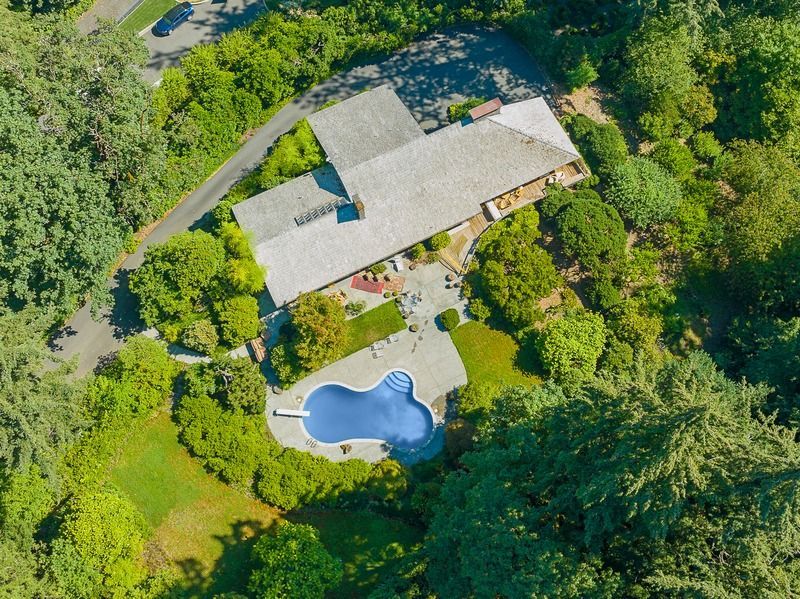Aerial view of a mid-century modern home with a pool, patio, and lush surrounding trees.