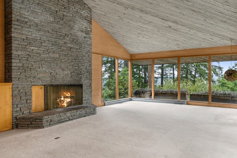 Living room with stone fireplace, large windows, and sloped ceiling.