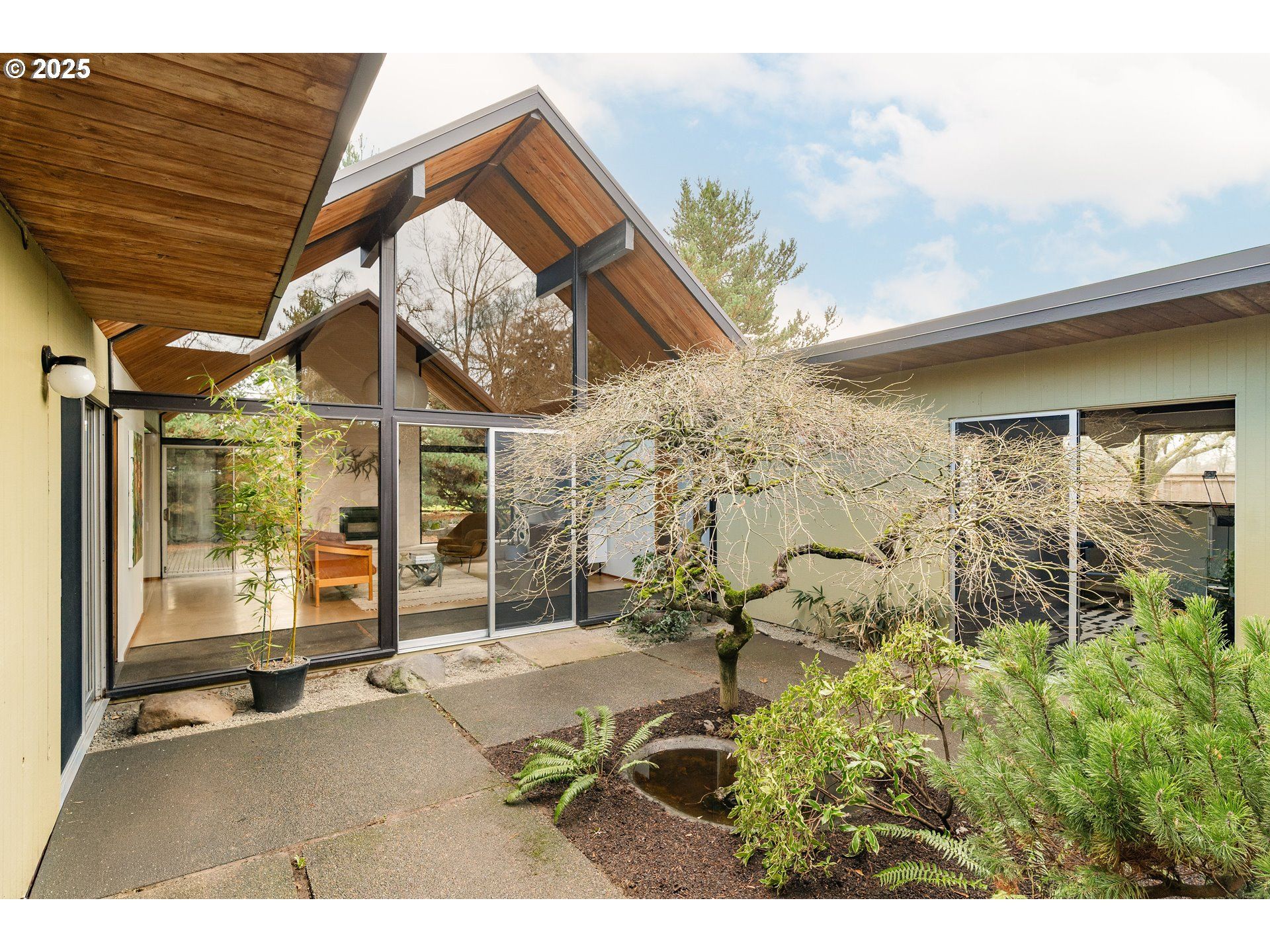 Mid-century modern home with large glass windows and an open courtyard with a flowering tree.