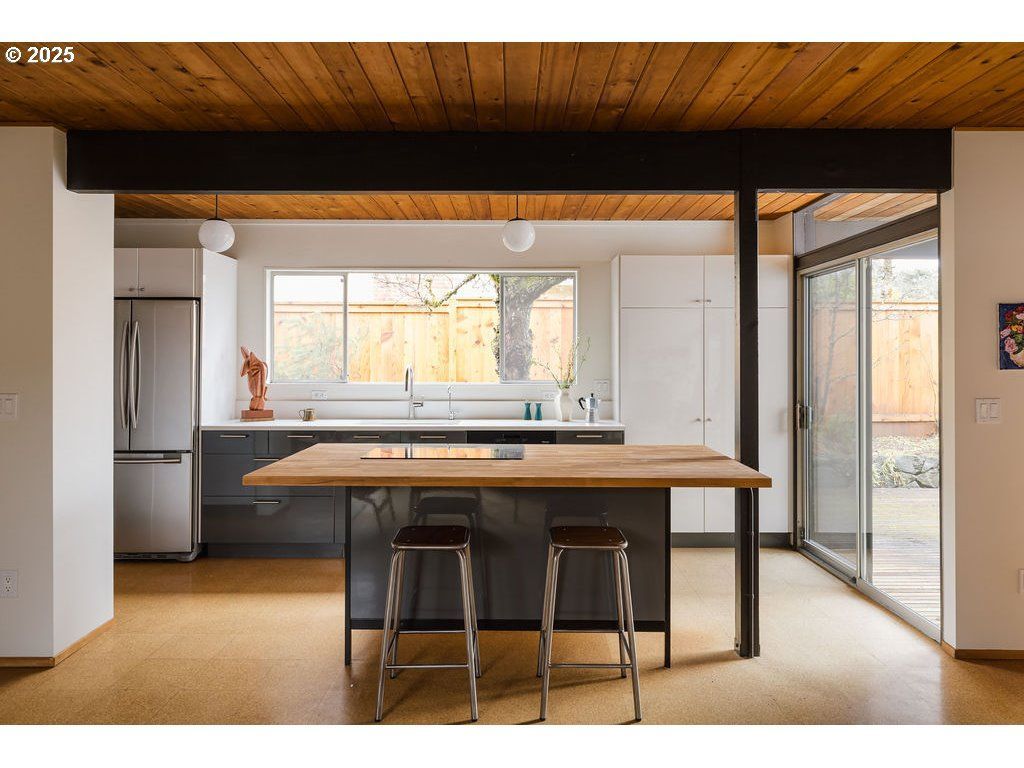 Kitchen with wood ceiling, island with stools, window, and sliding glass door.