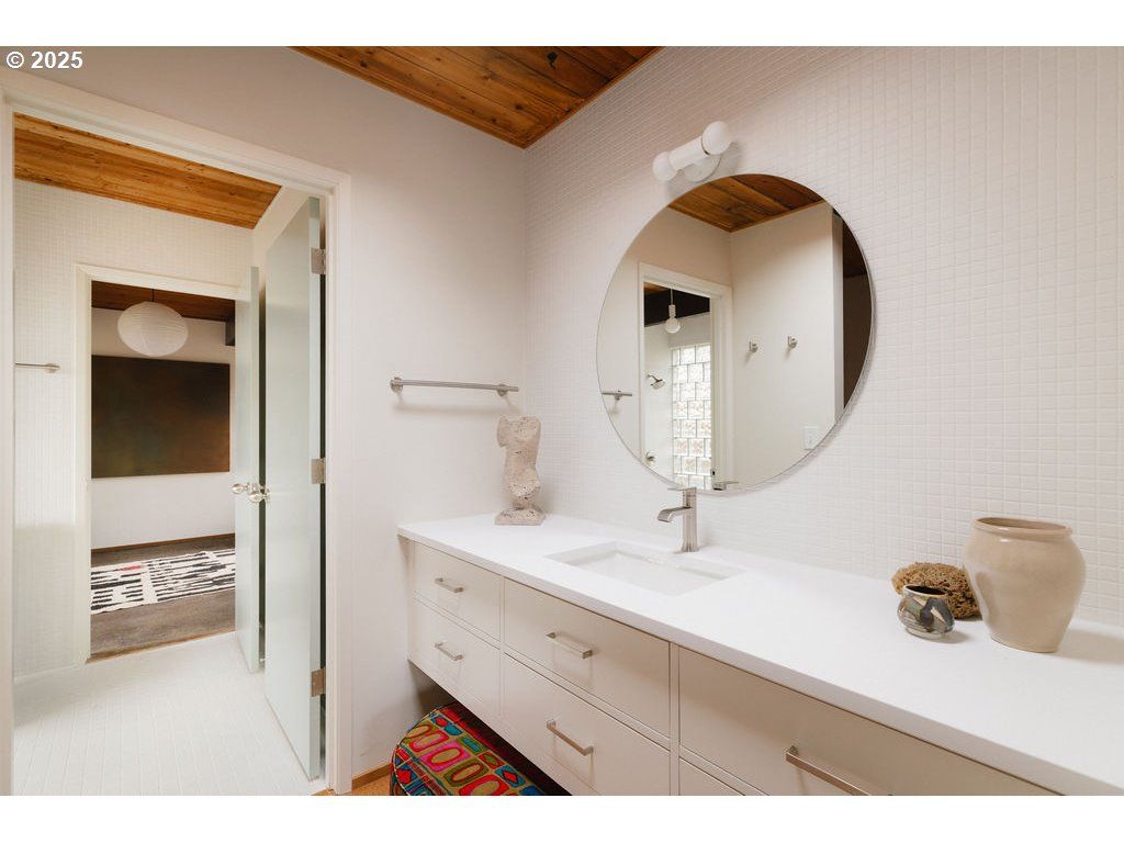 Bathroom with white vanity, round mirror, and doorway to another room.