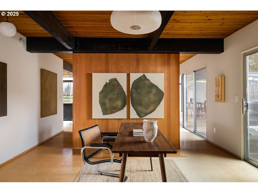Mid-century modern home office with desk, artwork, wood paneling, and large windows.