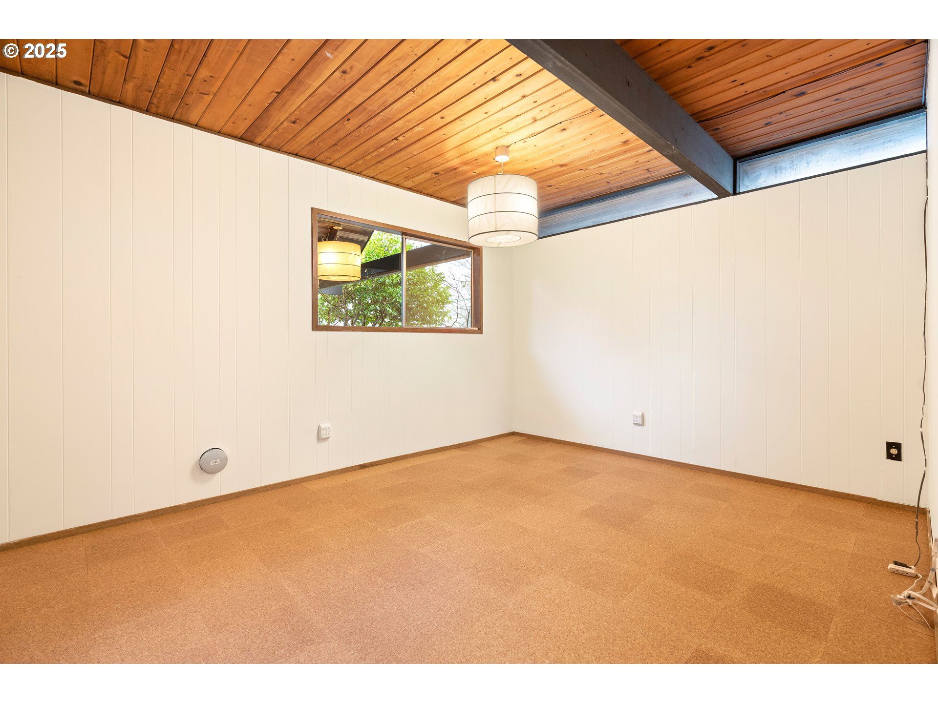 Empty room with paneled walls, wood ceiling, window, and carpet.