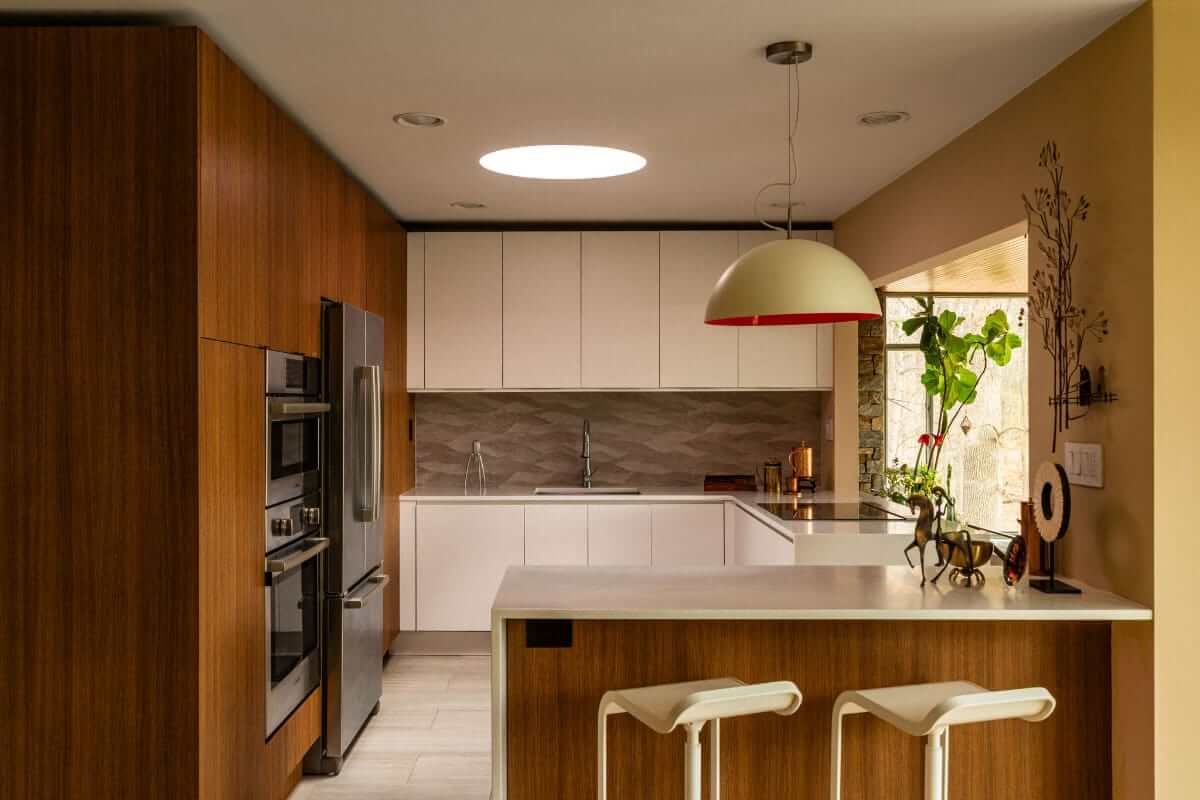 Modern kitchen with wood cabinets, white countertops, and a skylight. A hanging light and bar stools are also visible.