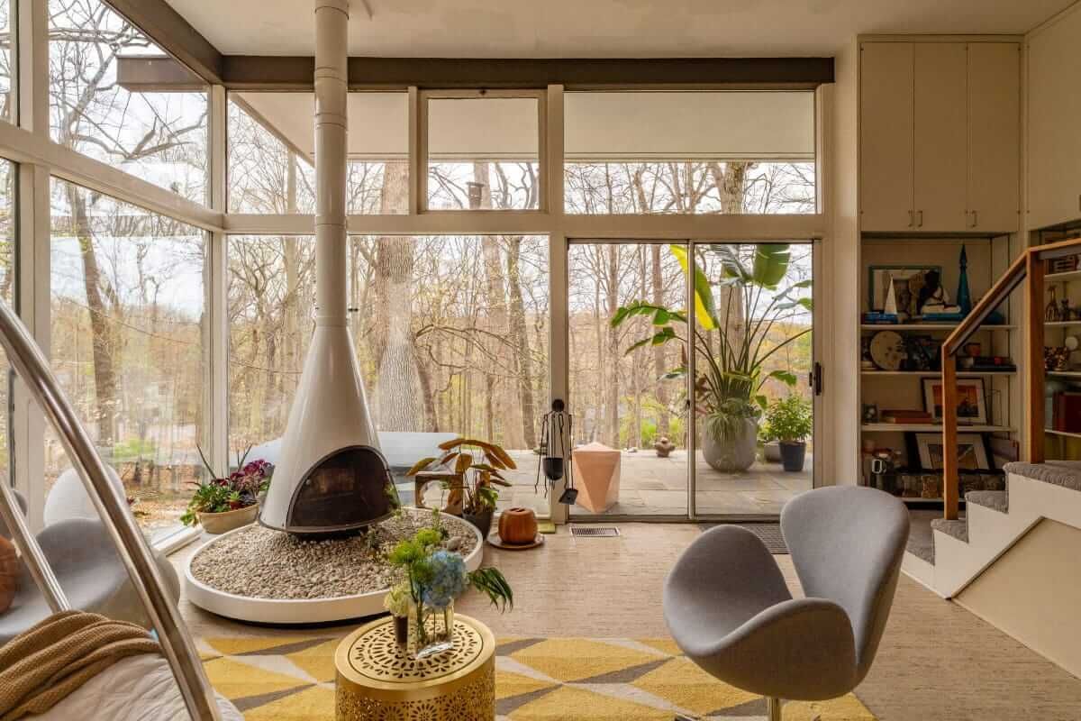 Modern living room with a unique fireplace, floor-to-ceiling windows, and nature views.