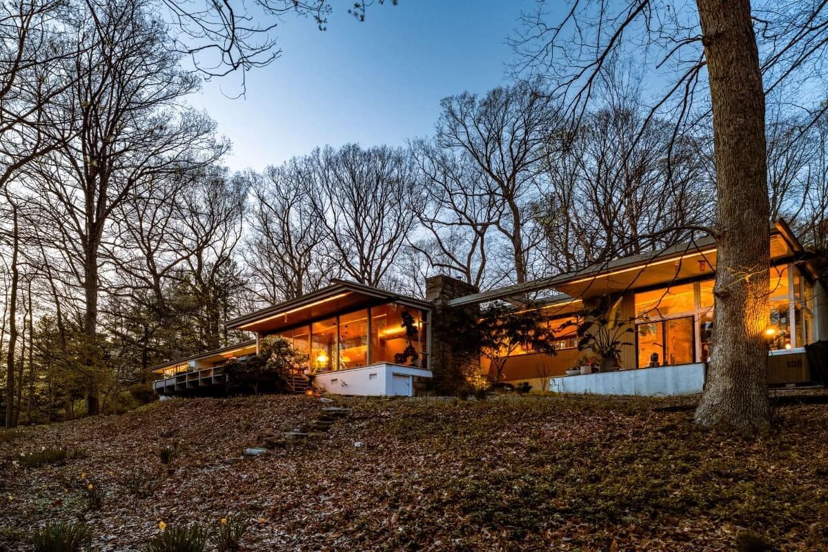 Modern home with large windows nestled amongst bare trees. The interior glows with warm light.