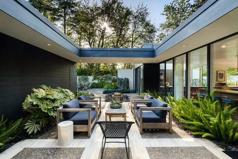 Courtyard with seating: blue cushions, wood frames, surrounding greenery, and open to garden.