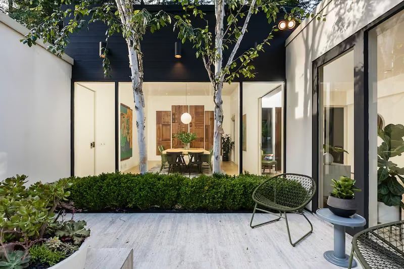 Courtyard with trees, patio furniture, and glass doors looking into a dining area.